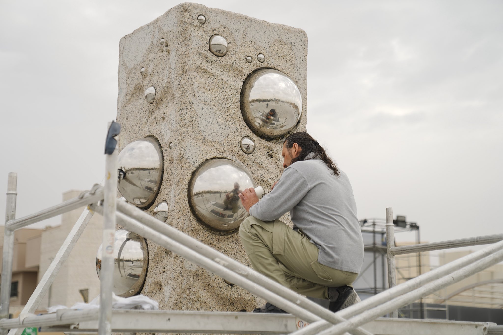 Artist working on a sculpture with reflective spheres at Tuwaiq Sculpture 2026 in Riyadh